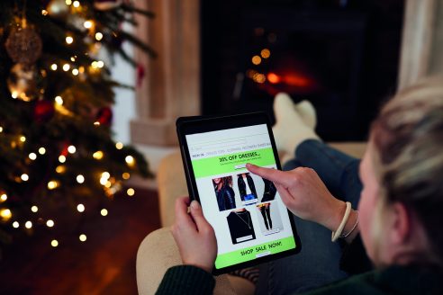 Woman At Home Using Digital Tablet To Shop For Clothes Online At Christmas